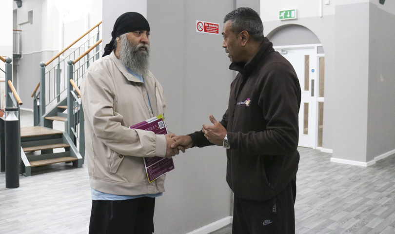 Two Individuals Shaking Hands Inside A Building With Stairs And A Railing In The Background