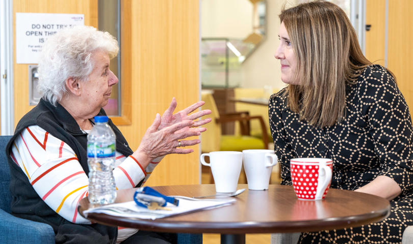 Two Women Speaking While Sat At A Table With Mugs