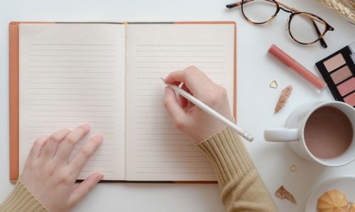 A person's hand holding a pencil over an open notebook