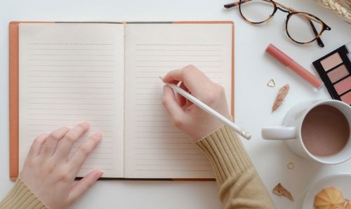 A persons hand holding a pencil over an open notebook