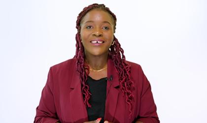 Woman With Curly, Braided Hair Smiling To Camera Wearing A Red Jacket And Black Top
