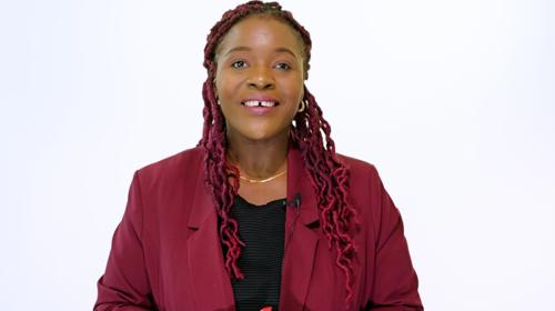 Woman With Curly, Braided Hair Smiling To Camera Wearing A Red Jacket And Black Top