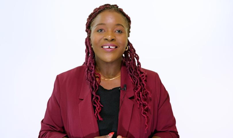 Woman With Curly, Braided Hair Smiling To Camera Wearing A Red Jacket And Black Top