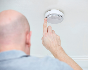 Image shows a man testing his smoke alarm by pushing the test button