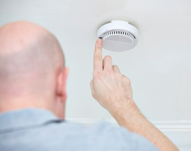 Image shows a man testing his smoke alarm by pushing the test button