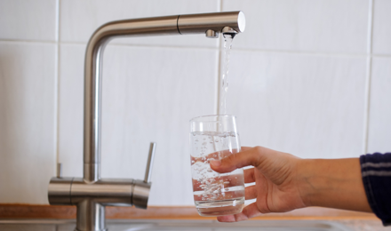 A person pouring a glass of water from the tap