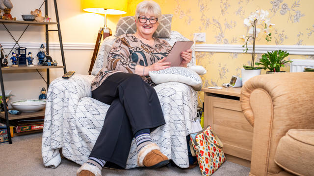 A Woman Smiling In Her Armchair While Holding A Tablet