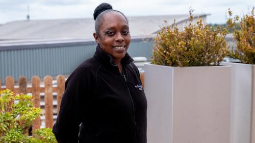 Smiling Woman In A Black Jacket With Hair Tied In A Bun Stood Outdoors