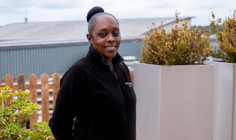 Smiling Woman In A Black Jacket With Hair Tied In A Bun Stood Outdoors