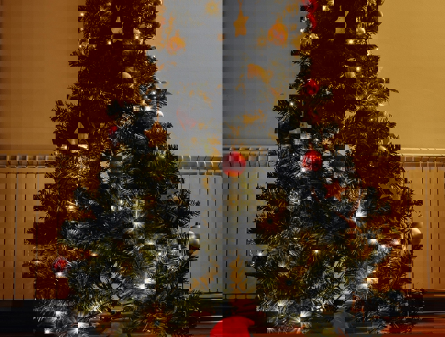 Close Up Of A Decorated Christmas Tree With A Doll In Front Of It Placed On The Floor