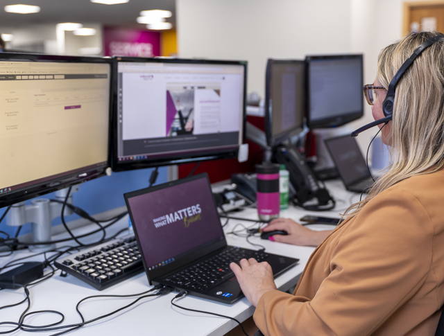 Person Wearing A Headset Working At A Multi Screen Computer Setup In An Office Environment