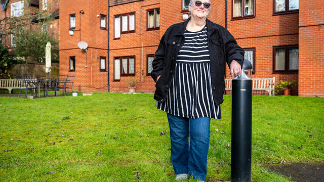 Woman leaning on light outside her a block of flats