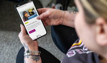 A Person With Tattoos Holds A Smartphone Displaying A Page Titled How We'll Contact You, Featuring A Smiling Person