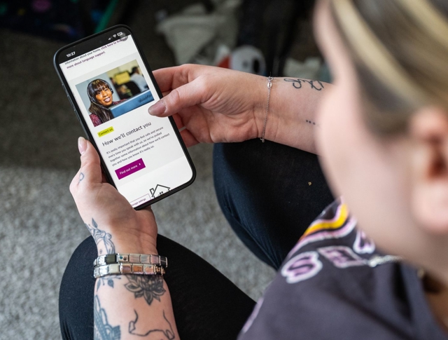 A Person With Tattoos Holds A Smartphone Displaying A Page Titled How We'll Contact You, Featuring A Smiling Person
