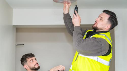 Two Repairs Operatives Fixing A Light For A Tenant