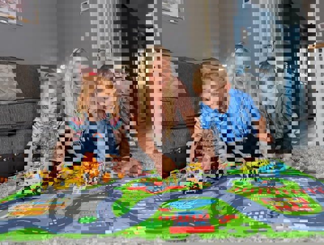 Mother Playing On The Floor With Her Daughter And Son With Toy Cars And Trucks