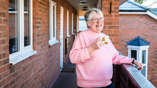A Woman Standing Outside Her Apartment With A Mug