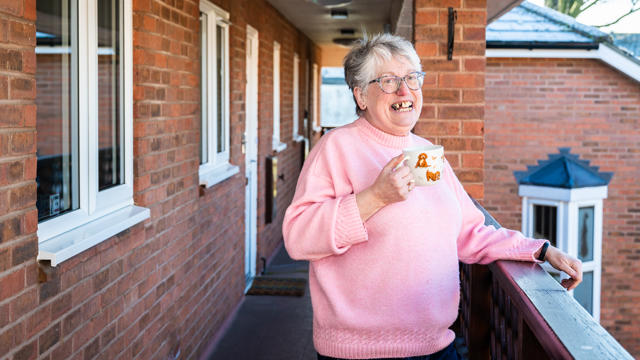 A Woman Standing Outside Her Apartment With A Mug
