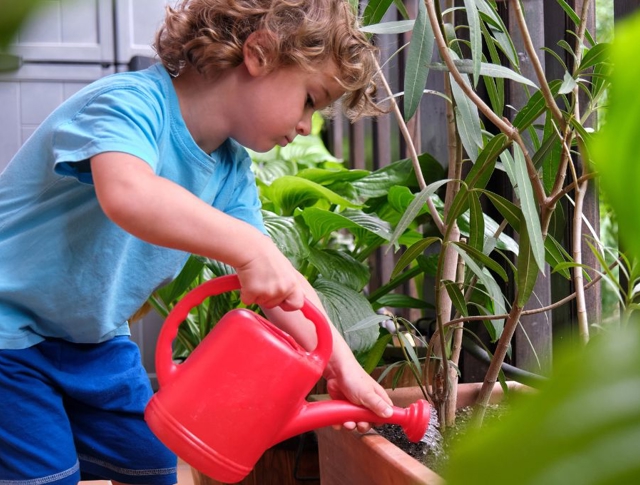 A child watering plants with a small plastic watering can
