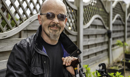Gary Sitting Outside Of His Home With Aids And Adaptations