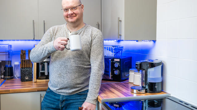 A Man Standing In His Kitchen With A Mug (1)