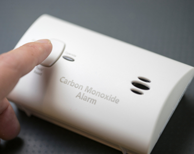 Image shows someone pushing the test button on a carbon monoxide alarm