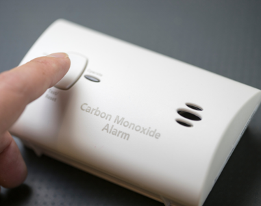 Image shows someone pushing the test button on a carbon monoxide alarm