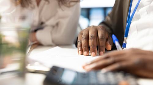 Two People Completing Paperwork With A Calculator And Pen