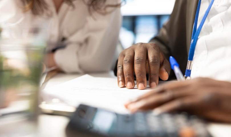 Two People Completing Paperwork With A Calculator And Pen