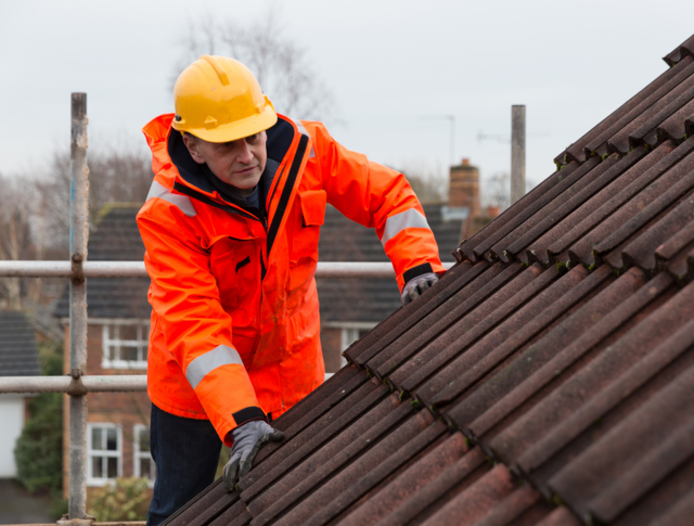 A person in high visibility clothing and a helmet inspecting a roof