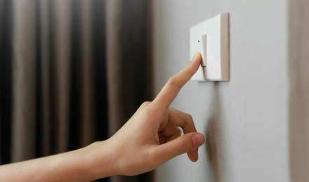 A person pressing a light switch on the wall