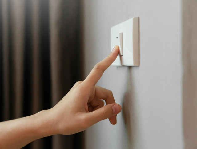 A person pressing a light switch on the wall