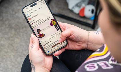 A Person Holding A Smartphone, Looking At A Facebook Feed