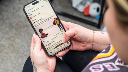 A Person Holding A Smartphone, Looking At A Facebook Feed