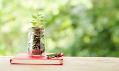 Jar Filled With Coins And A Plant Placed On A Red Book