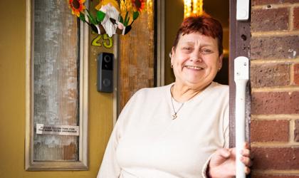 A Tenant Standing Outside Against Their Yellow Door, Holding A Handrail And Smiling