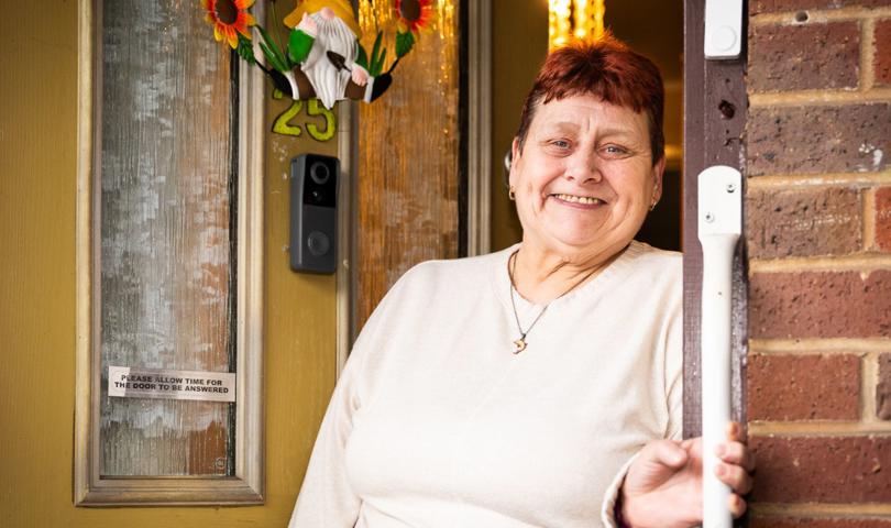 A Tenant Standing Outside Against Their Yellow Door, Holding A Handrail And Smiling