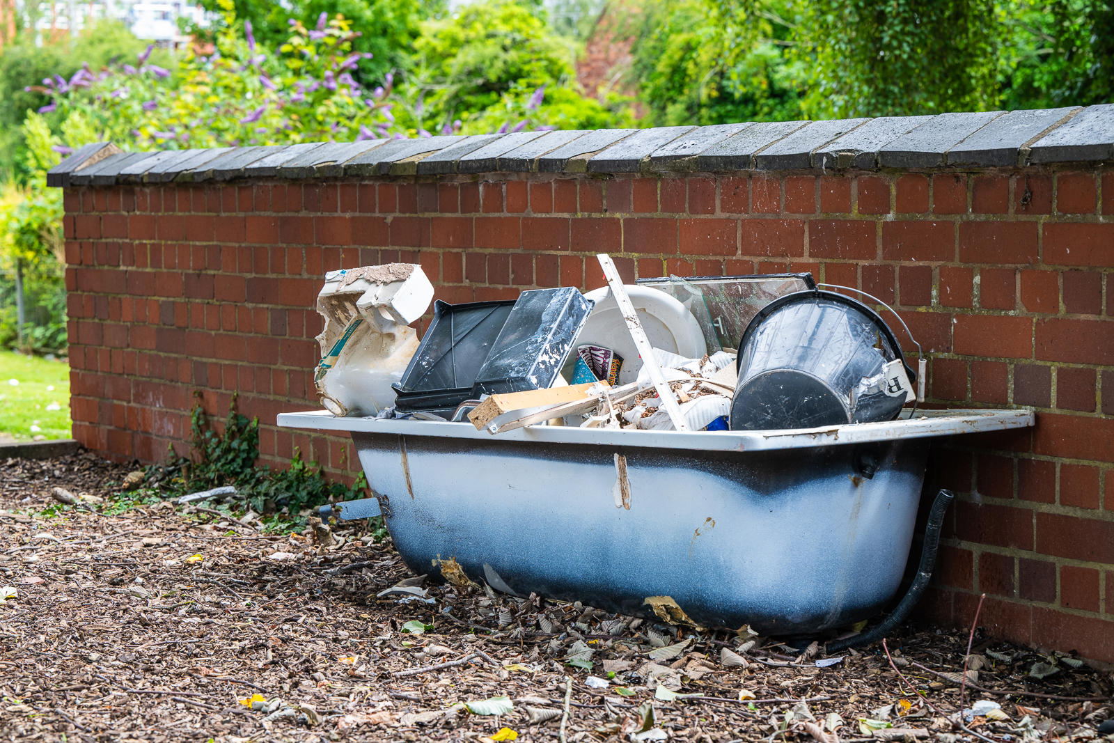 An Old Bathtub Filled With Rubbish, Sitting Against A Red Brick Wall