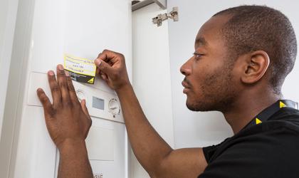 Engineer In A Black T Shirt Wearing A Lanyard Applying Annual Service Sticker To A Boiler