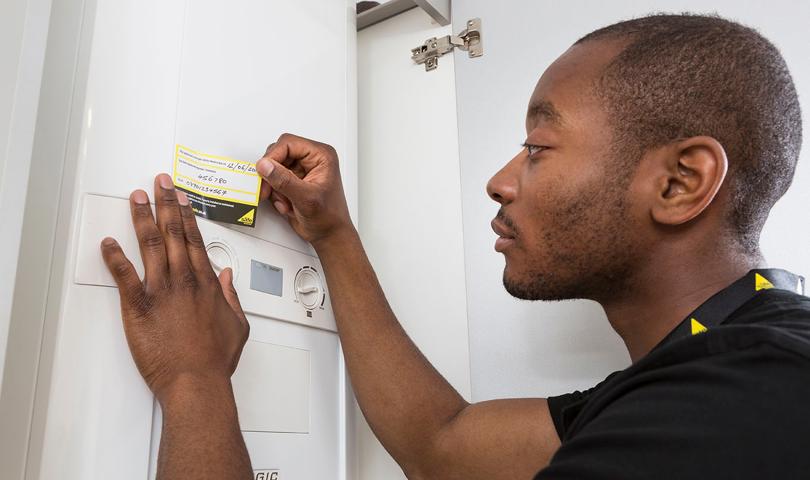 Engineer In A Black T Shirt Wearing A Lanyard Applying Annual Service Sticker To A Boiler