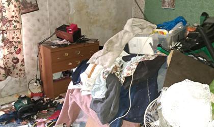 Cluttered Room With Piles Of Clothing, Household Items And Belongings Stacked Across The Floor