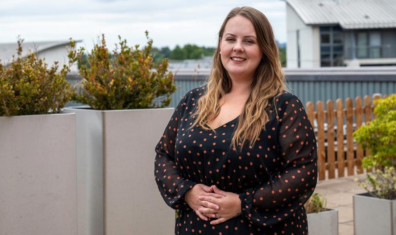 Woman Stood Outdoor In A Black Dress With Red Dots Smiling At The Camera