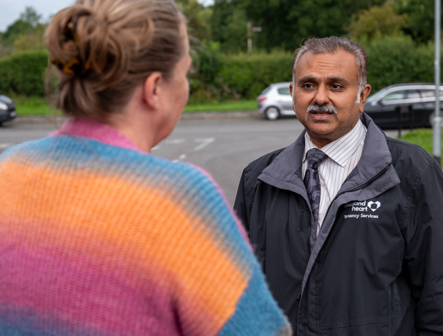 A Midland Heart employee with a clipboard speaking to 2 tenants