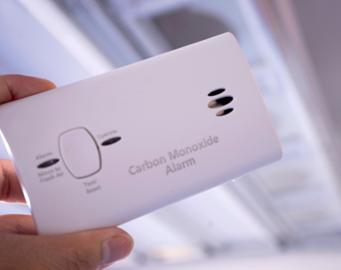 Image shows someone holding a carbon monoxide alarm