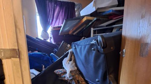 Small Room Filled With Stacked Suitcases, Framed Items, And Boxes Piled High, Blocking Access Near A Window With Curtains