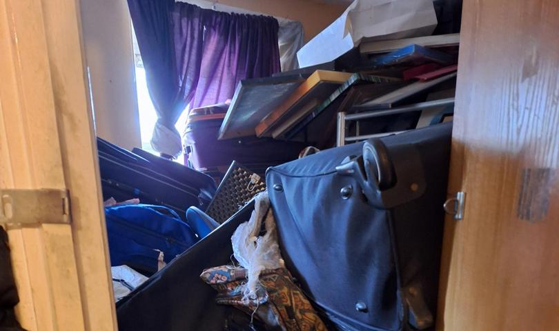 Small Room Filled With Stacked Suitcases, Framed Items, And Boxes Piled High, Blocking Access Near A Window With Curtains