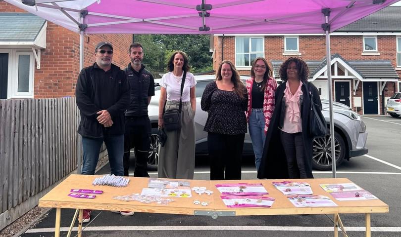 Group Of People Stood Smiling In Front Of A Table At An Event Under A Gazebo