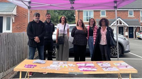 Group Of People Stood Smiling In Front Of A Table At An Event Under A Gazebo