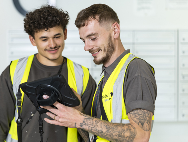 Electrician And An Apprentice Looking At A Tablet Computer