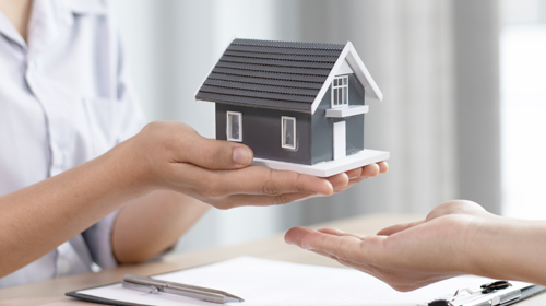 A person holding a miniature home to symbolise selling your home